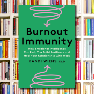 A photo of the front cover of the book Burnout Immunity against a background of bookshelves.