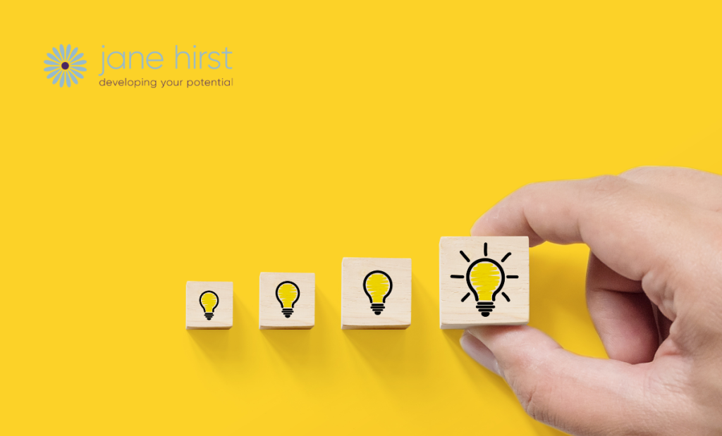 Against a yellow background is a row of four wooden cubes of increasing size. Each cube has a light bulb drawn on it. On the biggest cube, the light bulb is drawn to look like it has been switched on.